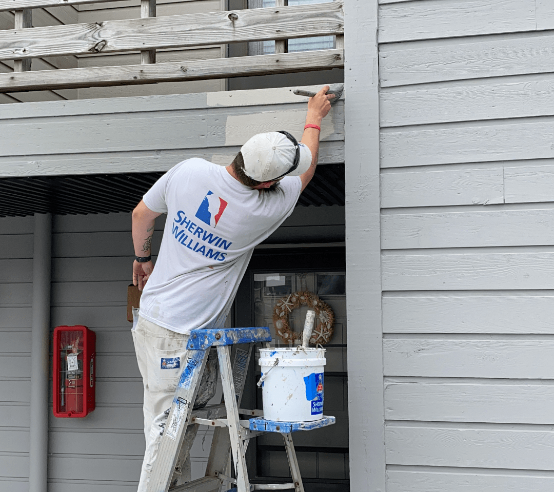 Painter on a ladder reaching to paint wood siding & trim on a condominium building in Avalon NJ